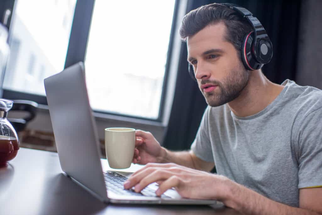 A man using a laptop with headphones and a cup of coffee.