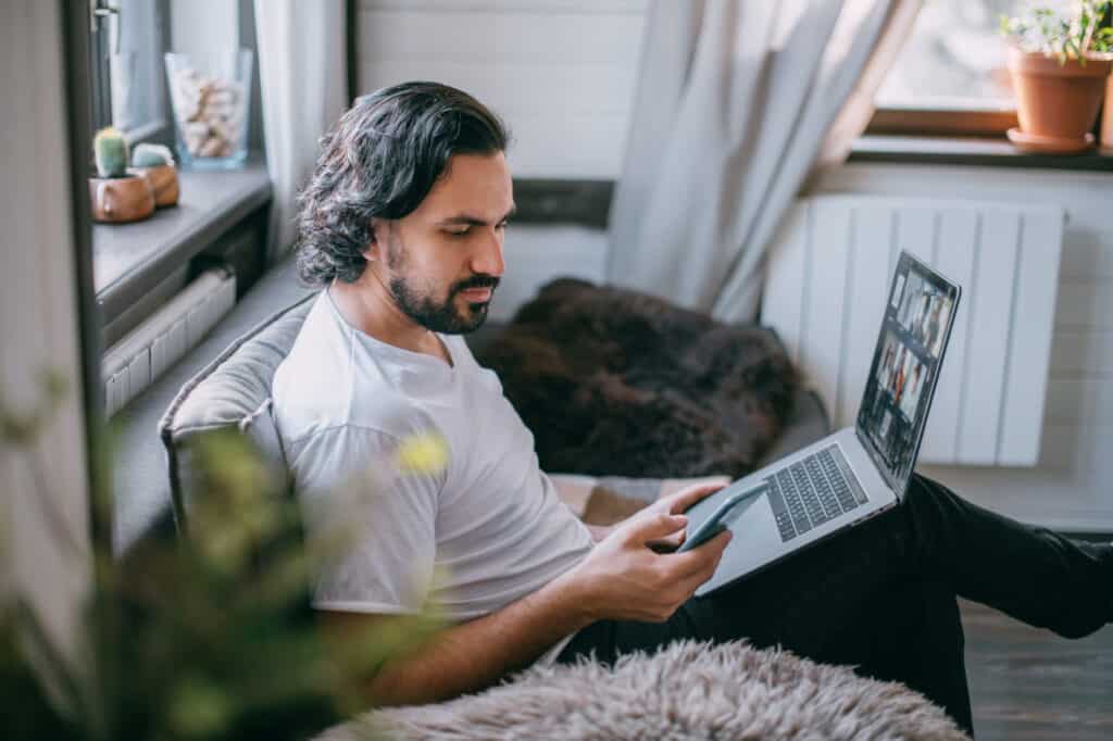 A man sitting on a couch using a laptop to research the best online business to start.