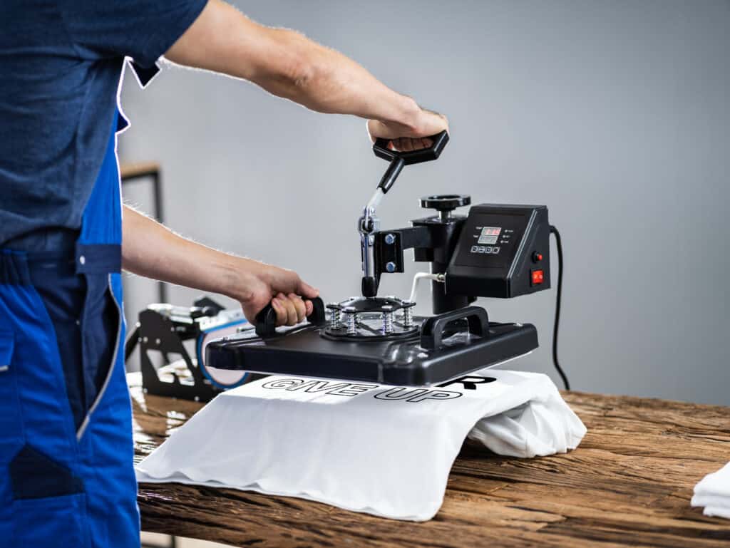A man is using a machine to make an on-demand t-shirt printing.