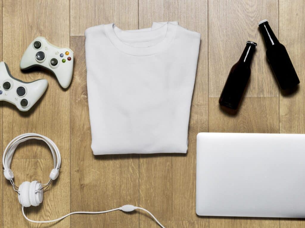 A white t - shirt featuring a unique design, accompanied by a laptop and headphones, resting on a wooden floor.