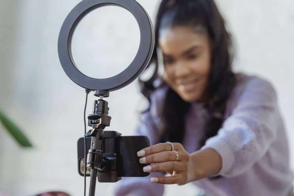 A woman using a ring light to take a selfie while starting a business podcast.