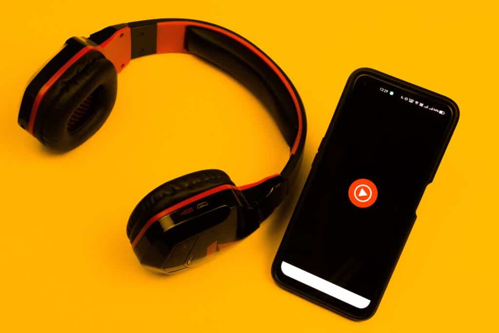 A pair of headphones and a phone on a yellow background, perfect for your podcasting business model.