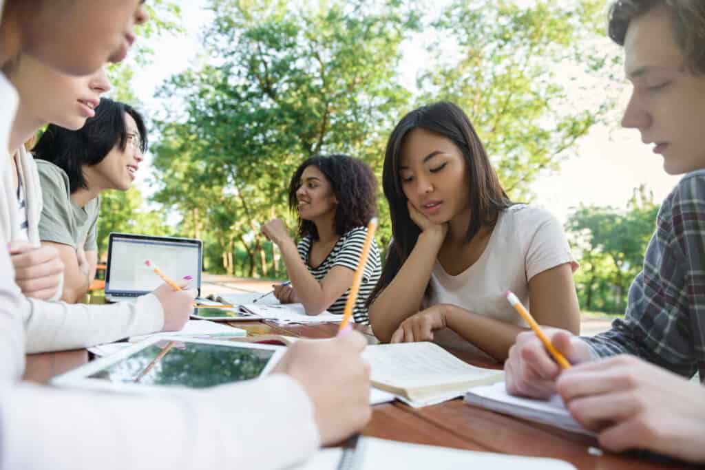 A group of young people sitting around a table in a park planning how to sell their courses online.