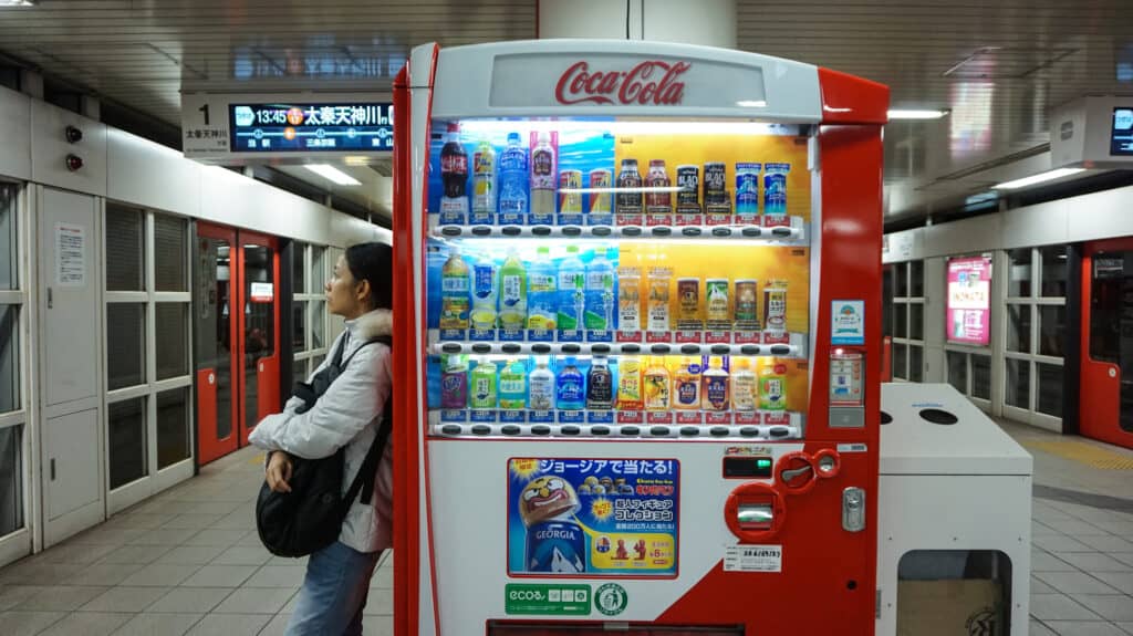 A person standing next to a brightly lit beverage vending machine, representing passive income businesses, in a subway station.