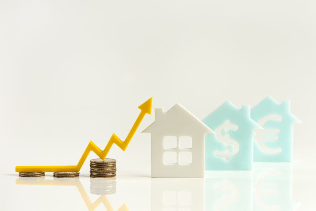 Rising real estate prices concept with coin stacks, house icons, and an upward trend arrow, illustrating online passive income ideas.