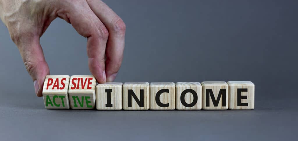 Hand flipping a wooden block, changing the word 'active' to 'passive' in the context of active income vs passive income, paired with the word 'income' on other blocks.