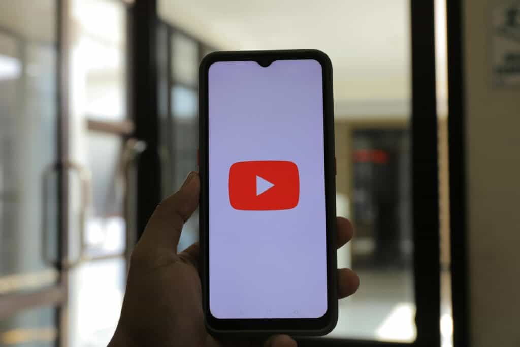 A person's hand holding a smartphone displaying online passive income ideas on the Youtube logo screen.