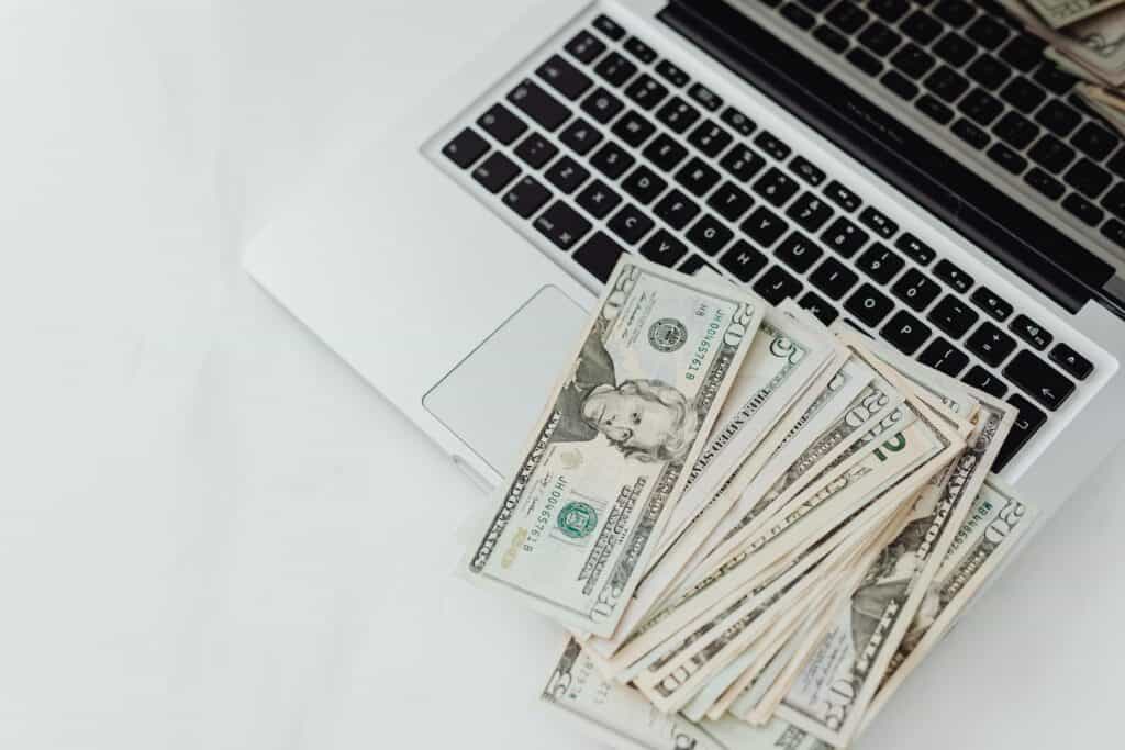 A laptop with a stack of US dollar bills symbolizing passive income from a franchise, resting on its keyboard.