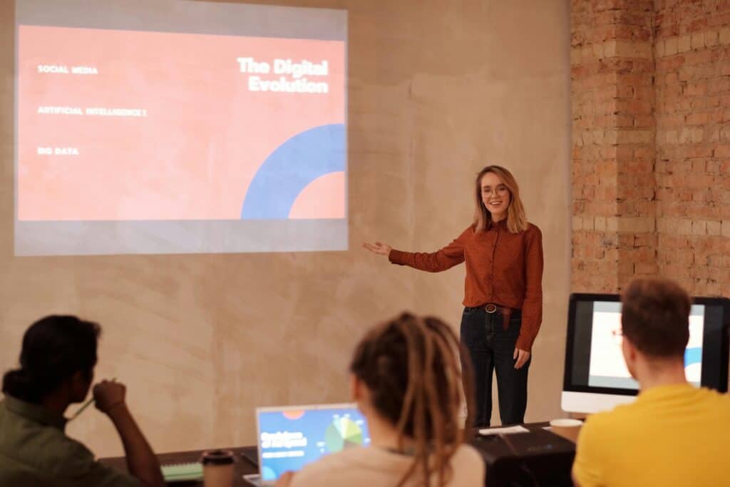 Woman presenting a digital evolution concept, emphasizing passive income businesses, on a screen to an audience during a workshop.