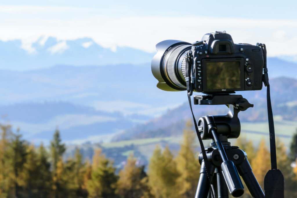 Dslr camera on a tripod capturing a scenic landscape with mountains in the background and illustrating how to make residual income from home.