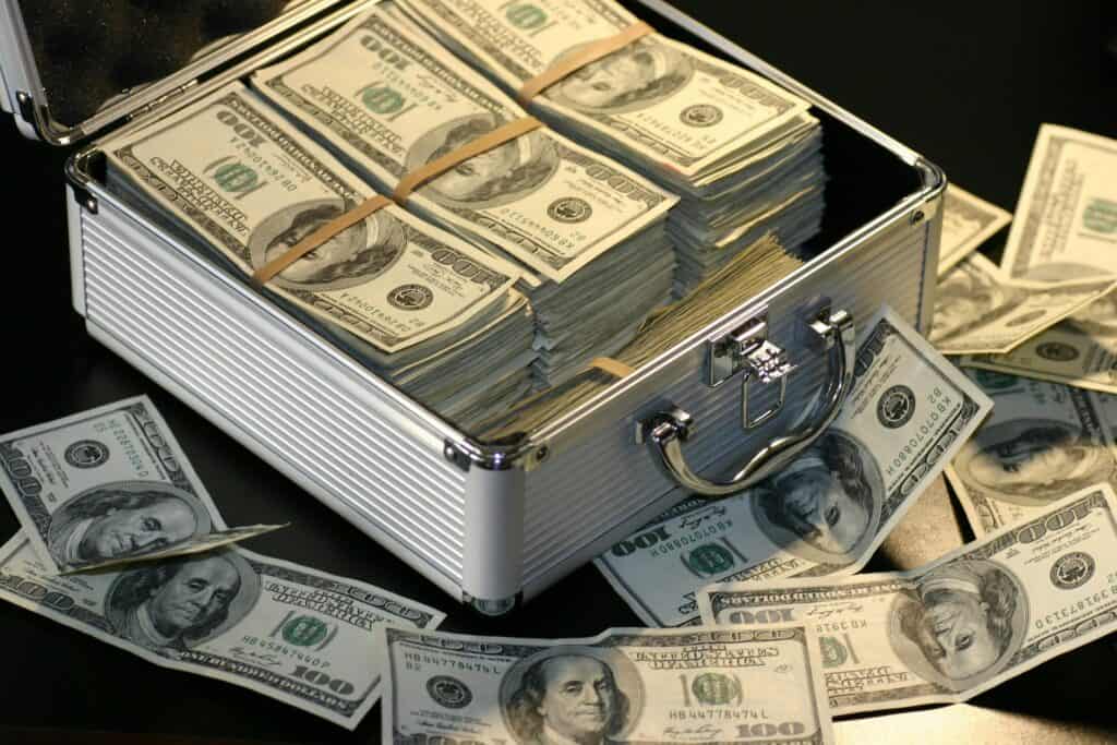 A silver briefcase, symbolizing a lucrative passive income franchise, overflowing with stacks of US hundred-dollar bills.
